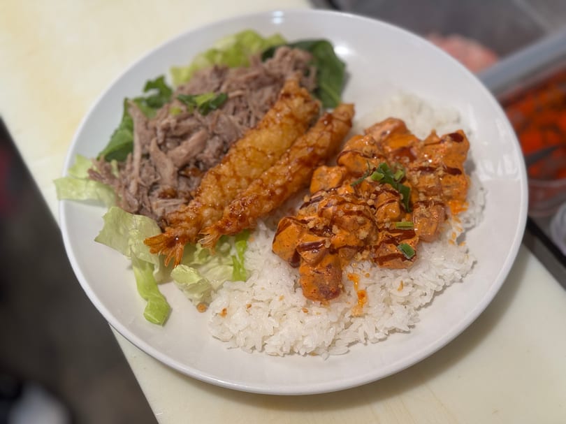 A white plate with rice, pulled pork, fried shrimp, and spicy salmon with sauce and green onions.